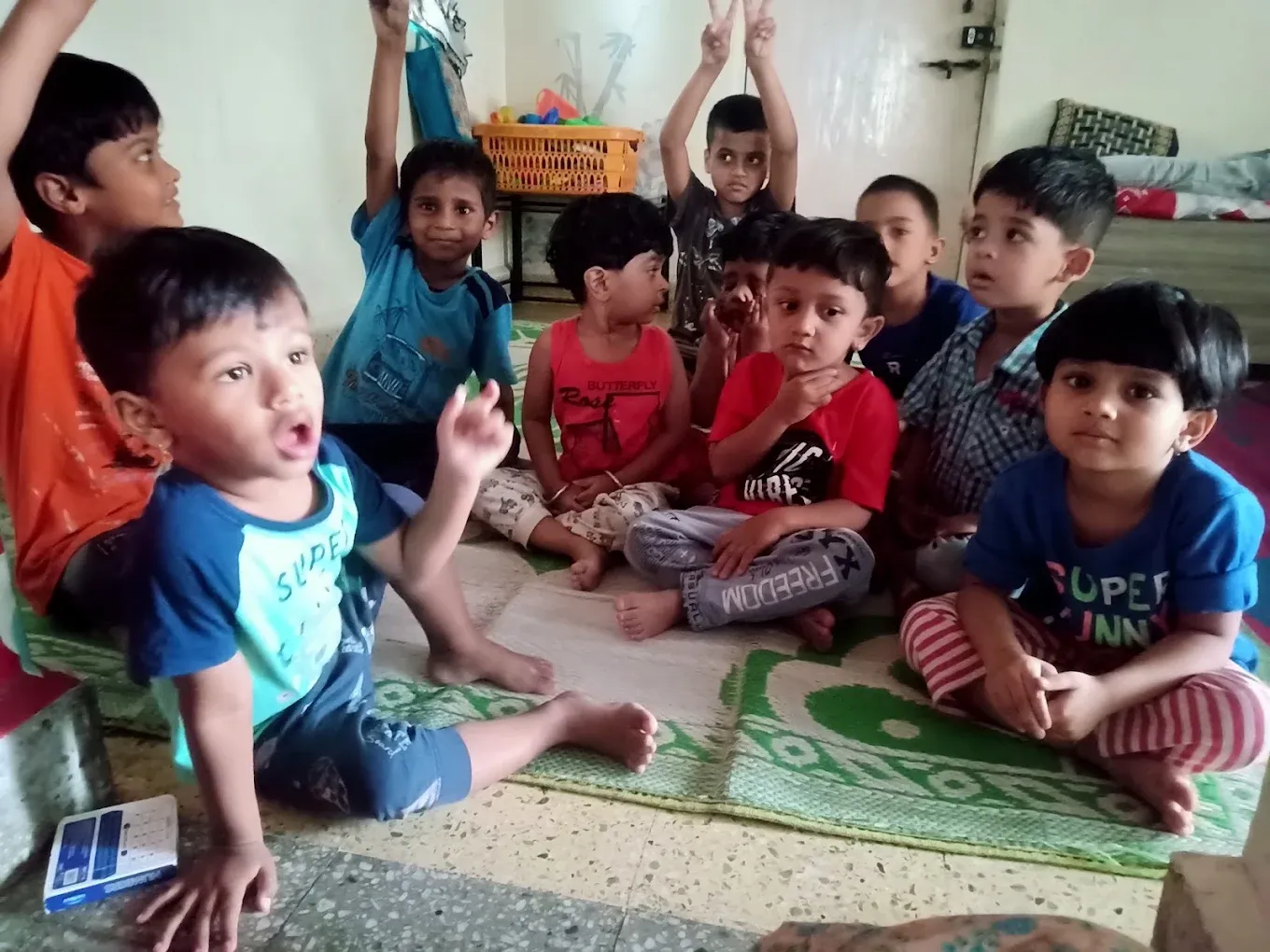 Children eagerly raising their hands during activity time at Maza Ghar