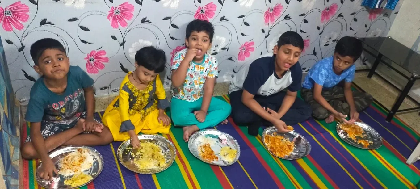 Children enjoying a home-cooked meal together on mats at Maza Ghar