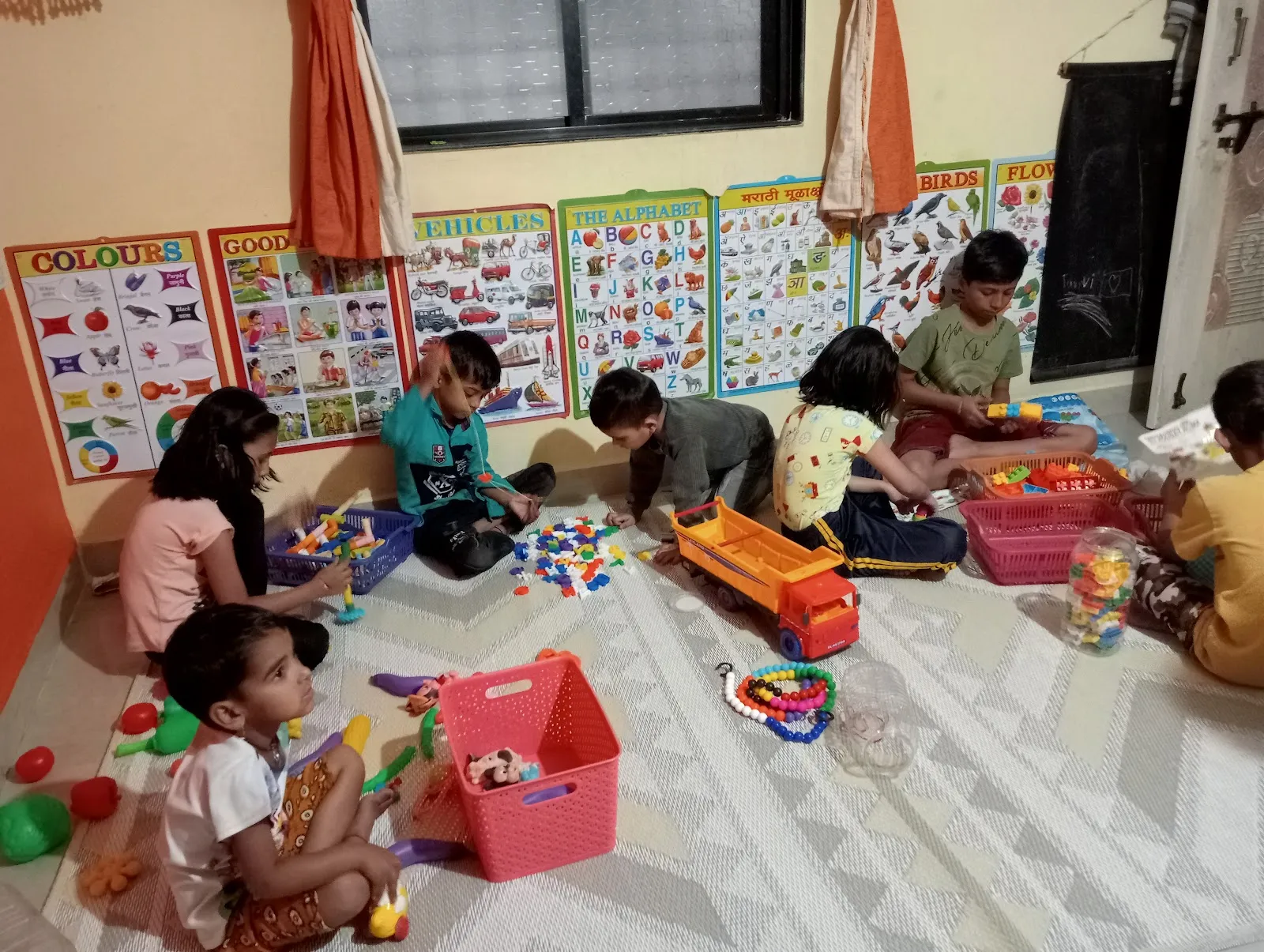 Children playing with blocks and toys in the Maza Ghar playroom surrounded by learning charts